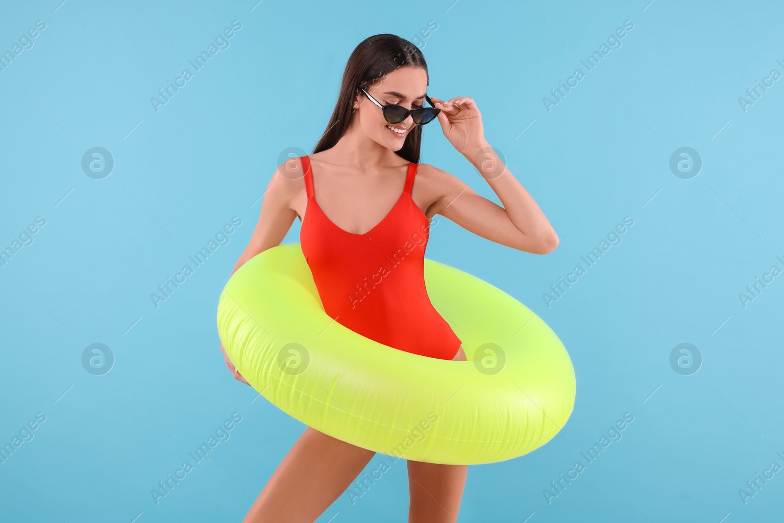 Photo of Young woman in stylish swimsuit with inflatable ring on light blue background