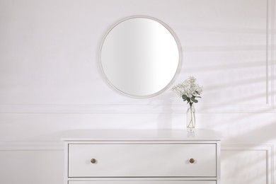 Trendy round mirror and chest of drawers near white wall. Interior element