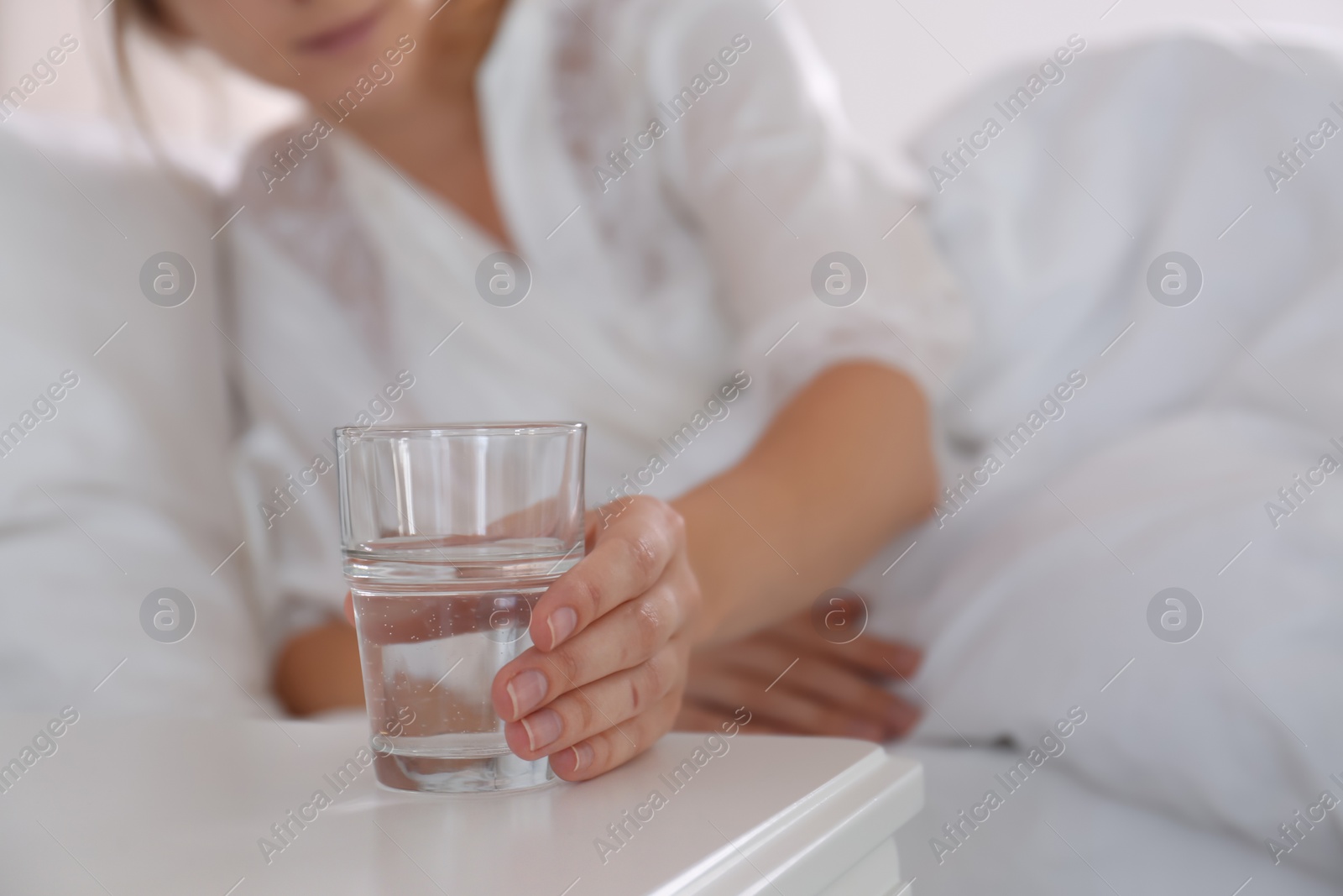 Photo of Woman taking glass of water from nightstand in bedroom, closeup