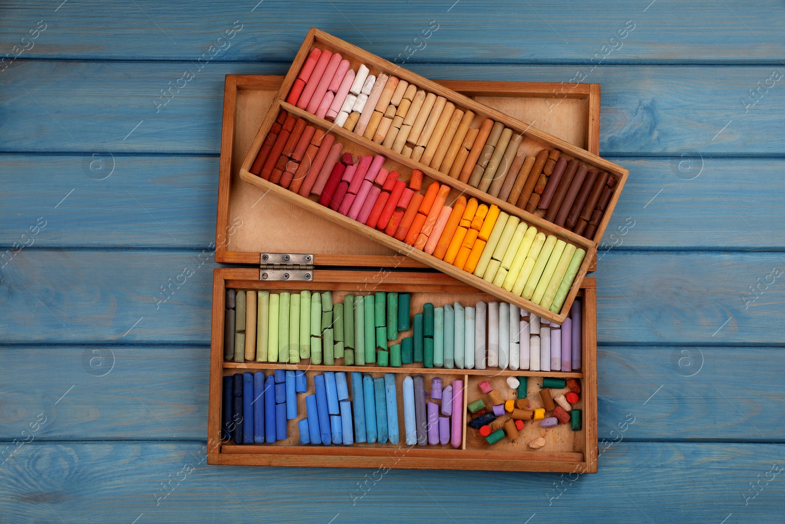 Photo of Drawing pastel set with box on light blue wooden background, top view