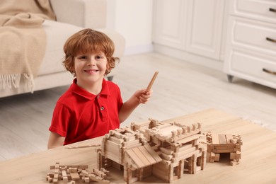 Photo of Cute little boy playing with wooden construction set at table in room, space for text. Child's toy