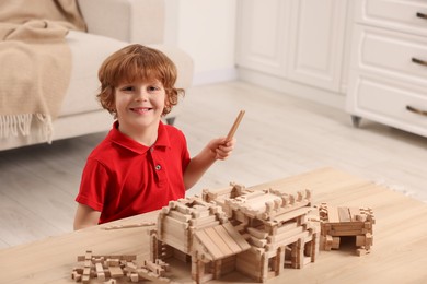 Cute little boy playing with wooden construction set at table in room, space for text. Child's toy