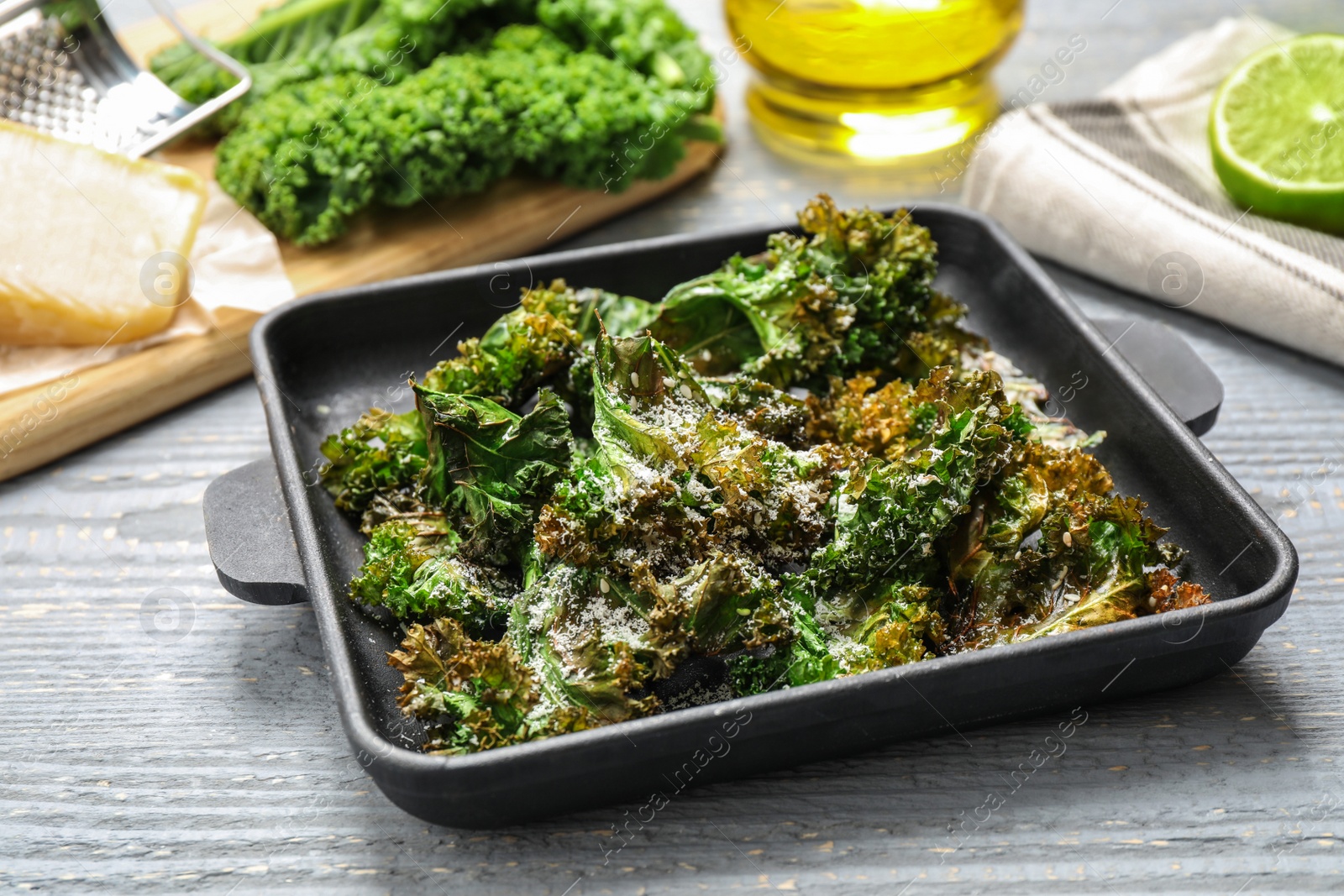 Photo of Tasty baked kale chips on grey wooden table