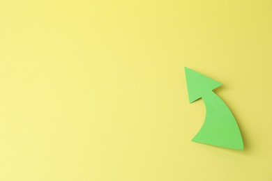 Curved green paper arrow on yellow background, top view. Space for text