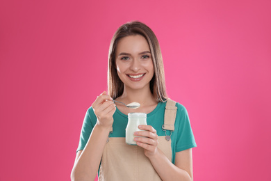 Young attractive woman with tasty yogurt on pink background