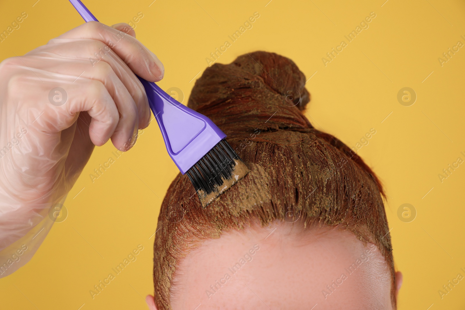 Photo of Young woman dyeing her hair with henna on yellow background, closeup