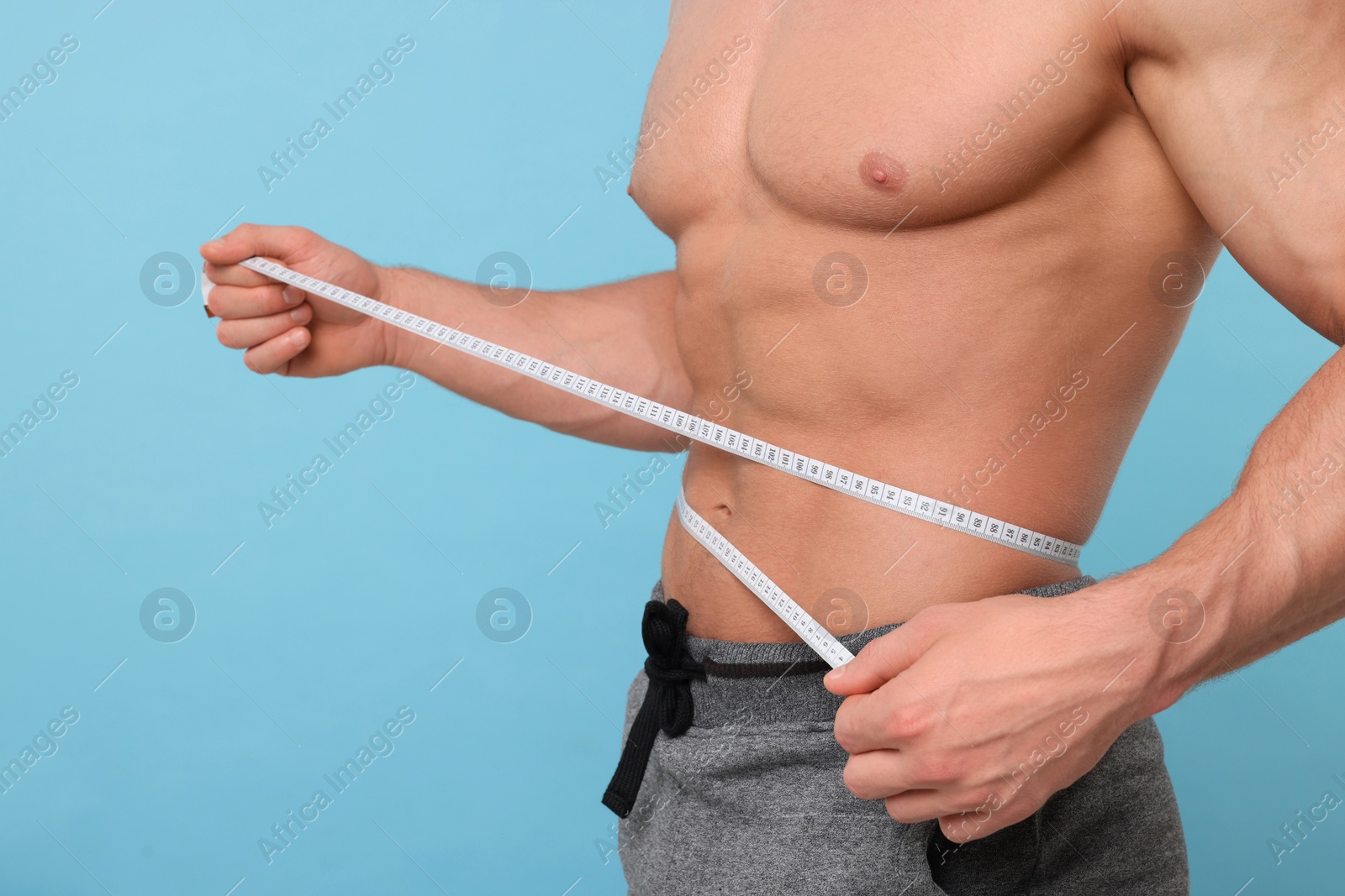 Photo of Athletic man measuring waist with tape on light blue background, closeup. Weight loss concept