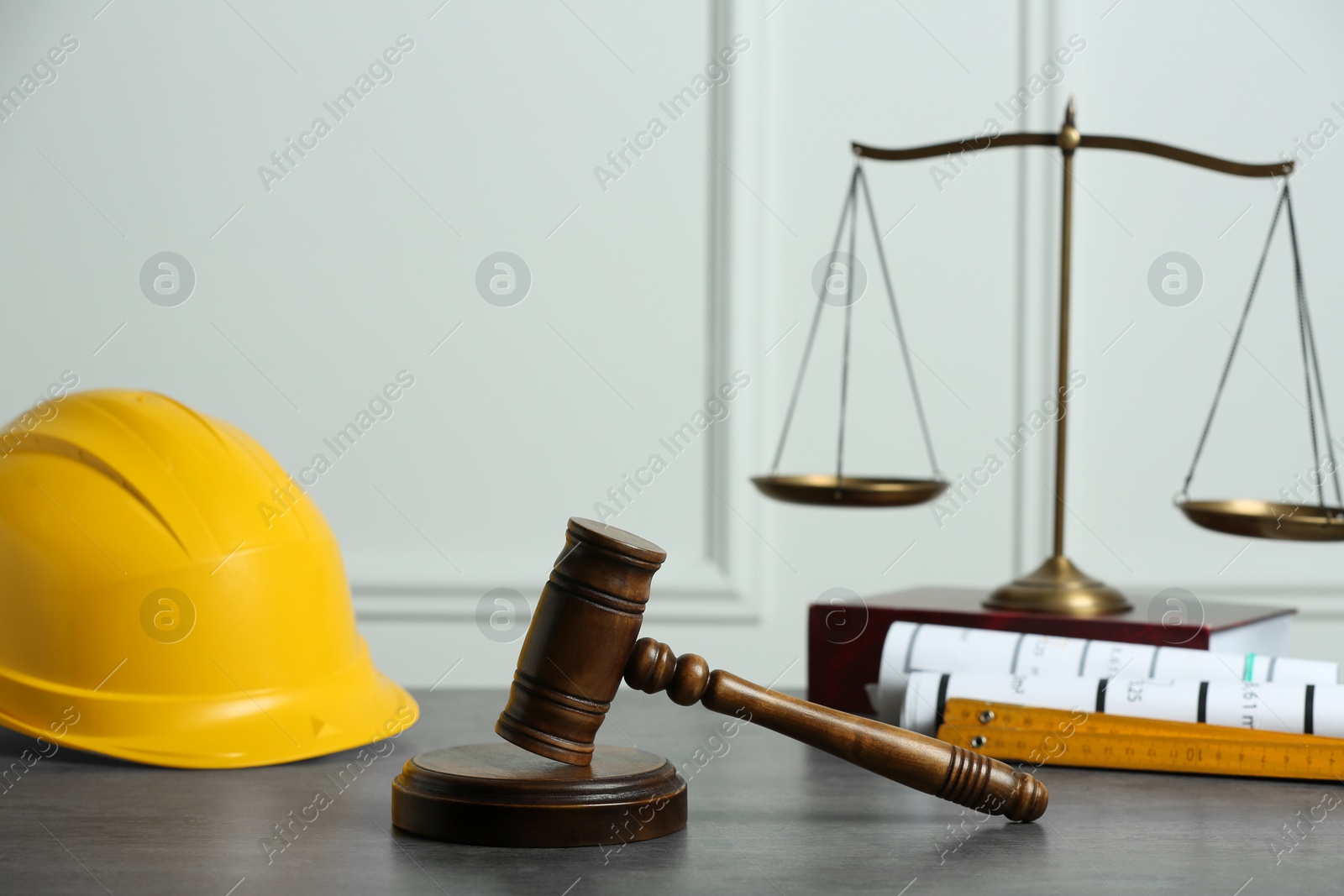 Photo of Construction and land law concepts. Judge gavel, scales of justice, protective helmet with drawings on grey table