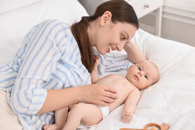 Happy young woman applying body cream onto baby`s skin on bed