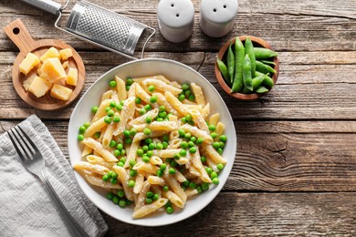 Delicious pasta with green peas, cheese, grater and fork on wooden table, top view. Space for text