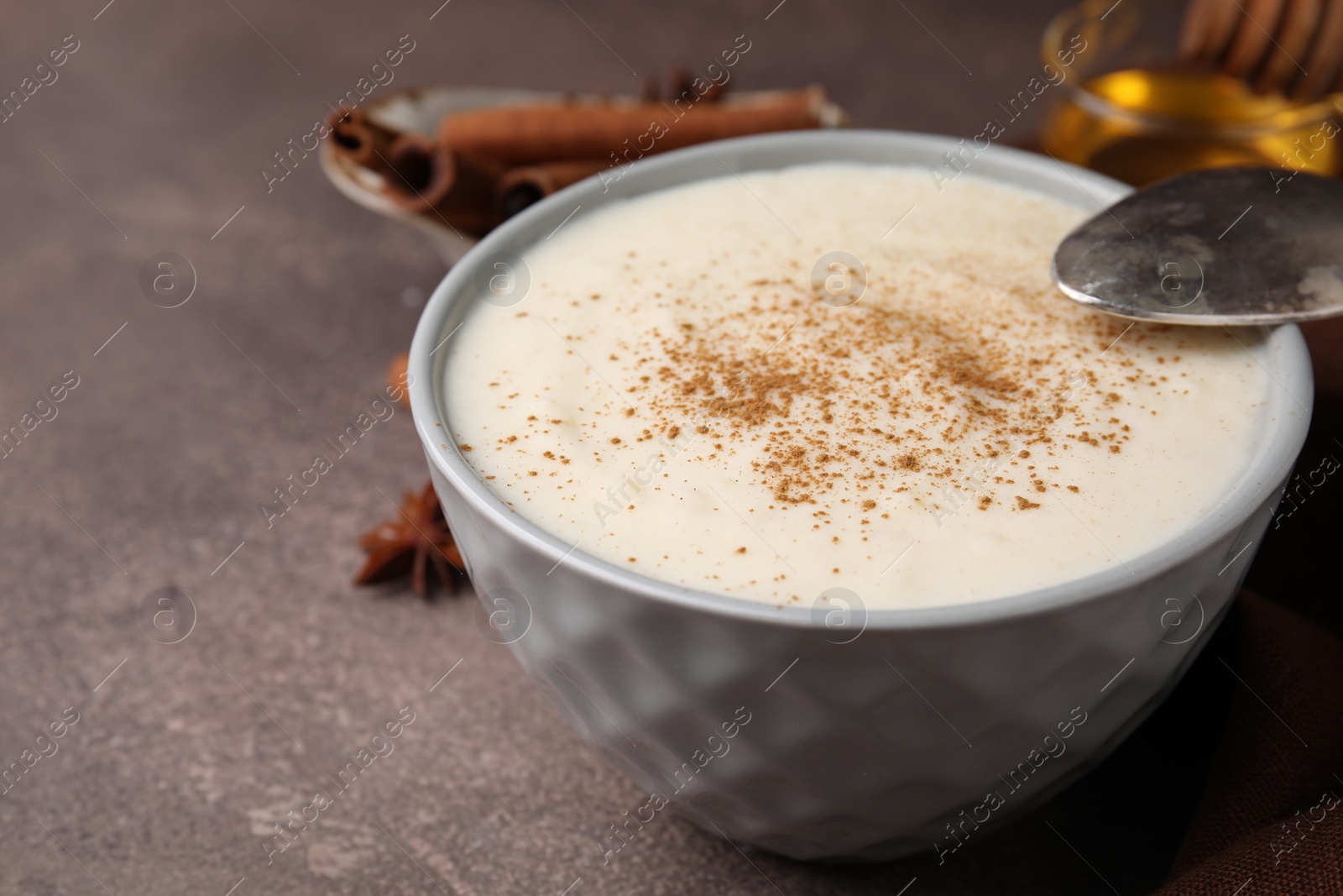Photo of Delicious semolina pudding with cinnamon in bowl and spoon on brown table, closeup. Space for text