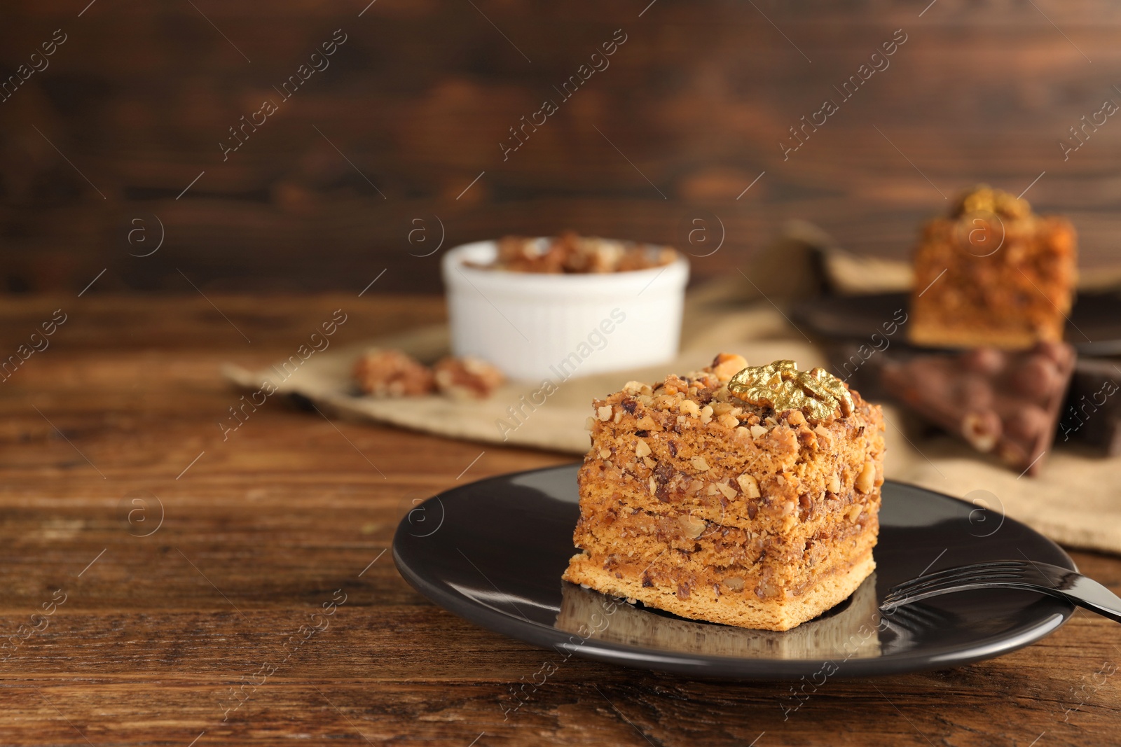 Photo of Piece of honey cake with walnuts and fork on wooden table, closeup with space for text