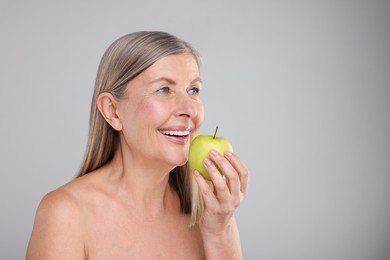 Photo of Beautiful woman with fresh apple on grey background, space for text. Vitamin rich food