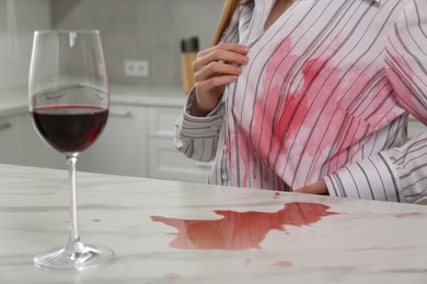 Photo of Woman with spilled wine over her shirt and marble table in kitchen, closeup