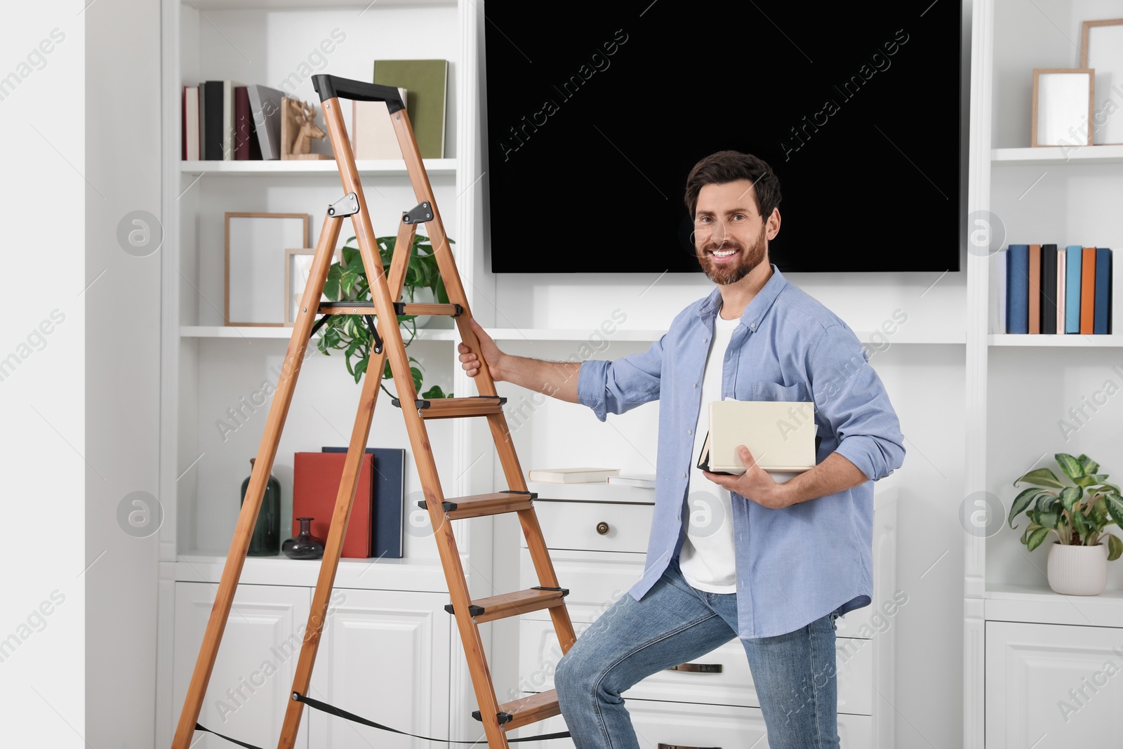 Photo of Happy man with books near wooden folding ladder at home