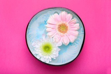 Beautiful composition with bowl of water and flowers on pink background, top view. Spa treatment