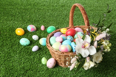 Photo of Wicker basket with Easter eggs and beautiful flowers on green grass