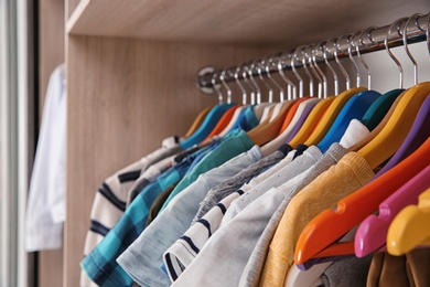 Photo of Stylish boy's clothes hanging in wardrobe, closeup