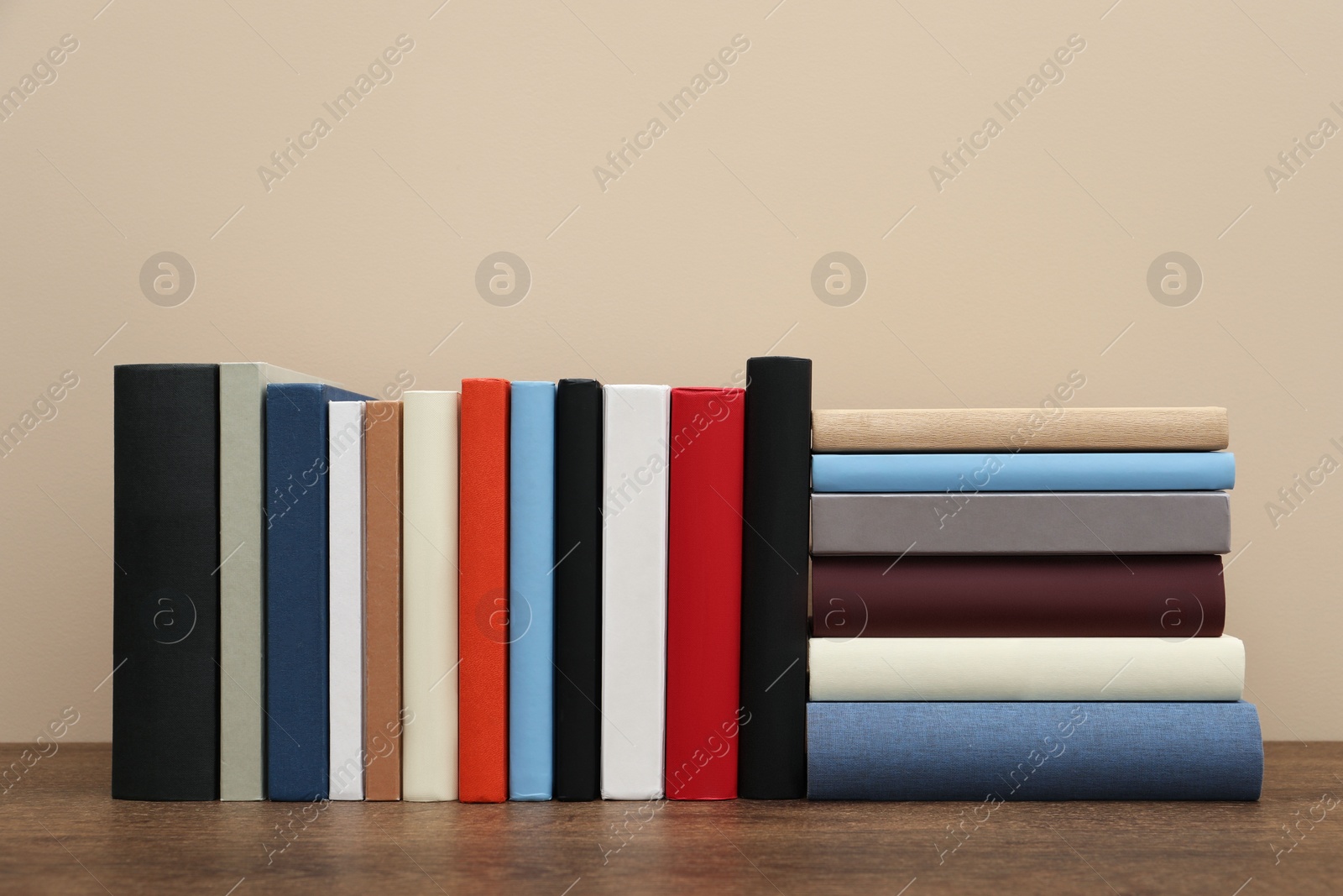 Photo of Many different hardcover books on wooden table near beige wall