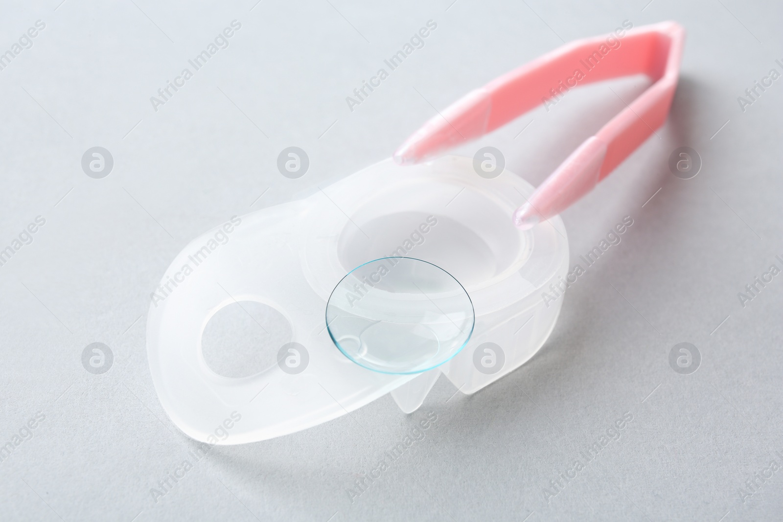 Photo of Package with contact lens and  tweezers on light background