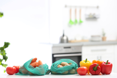 Photo of Net bags with vegetables on wooden table in kitchen