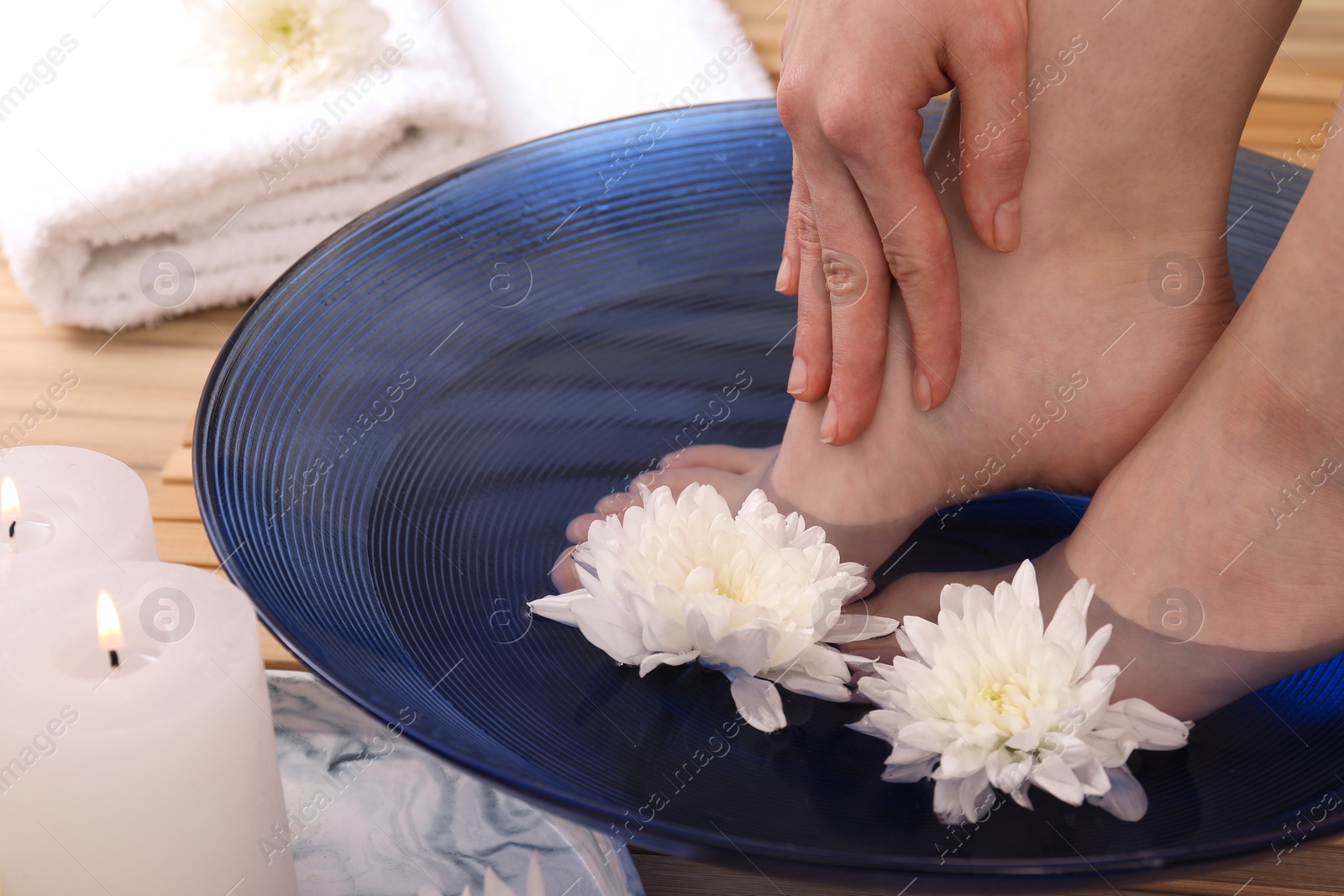 Photo of Woman soaking her feet in bowl with water and flowers on floor, closeup. Spa treatment