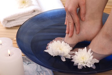 Photo of Woman soaking her feet in bowl with water and flowers on floor, closeup. Spa treatment