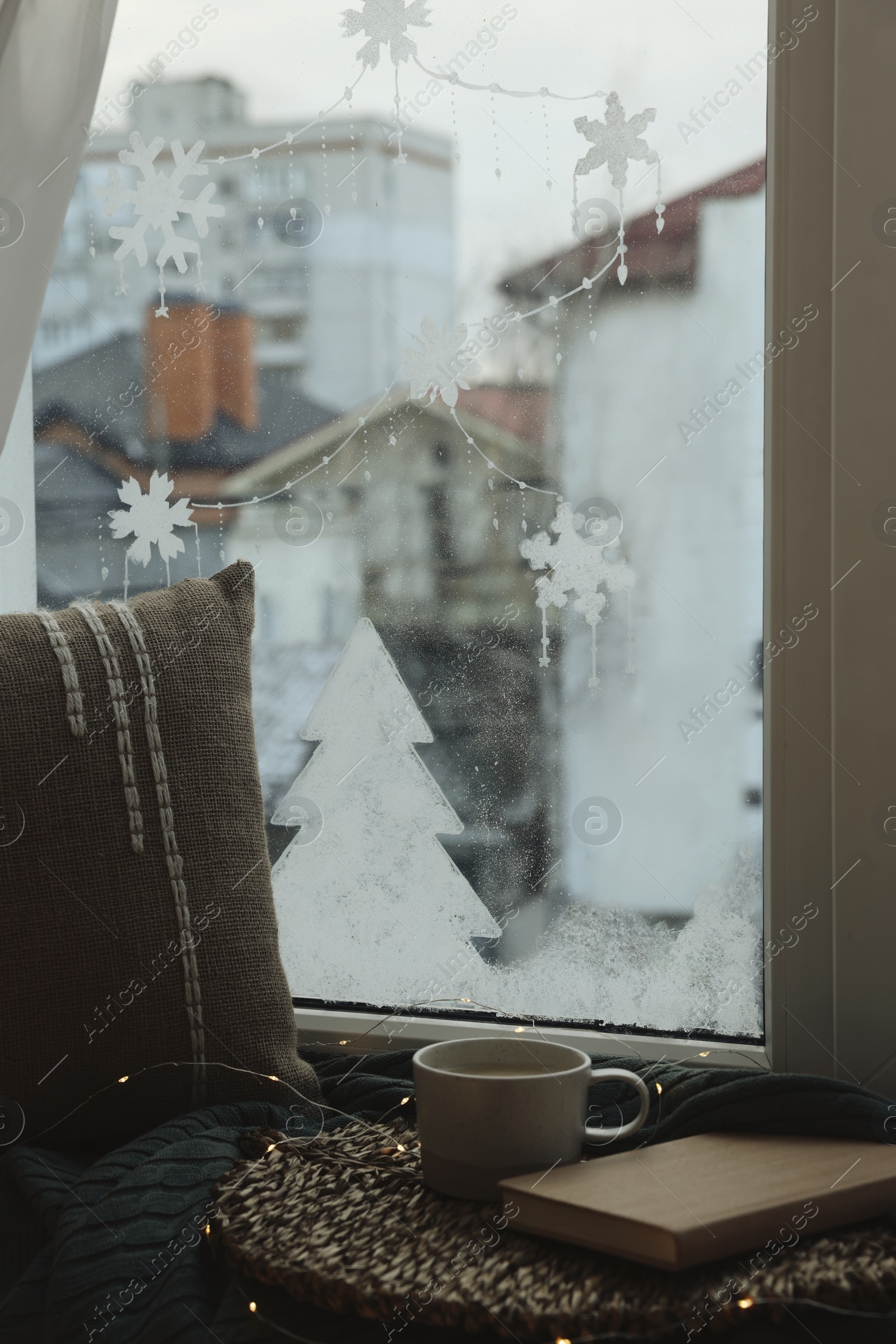 Photo of Cup of drink, book and beautiful drawing made with artificial snow on window at home. Christmas decor