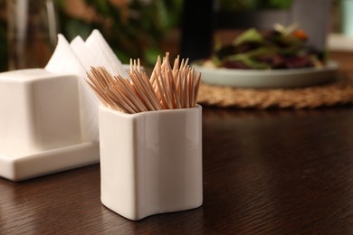 Photo of Holder with many toothpicks on wooden table, closeup. Space for text