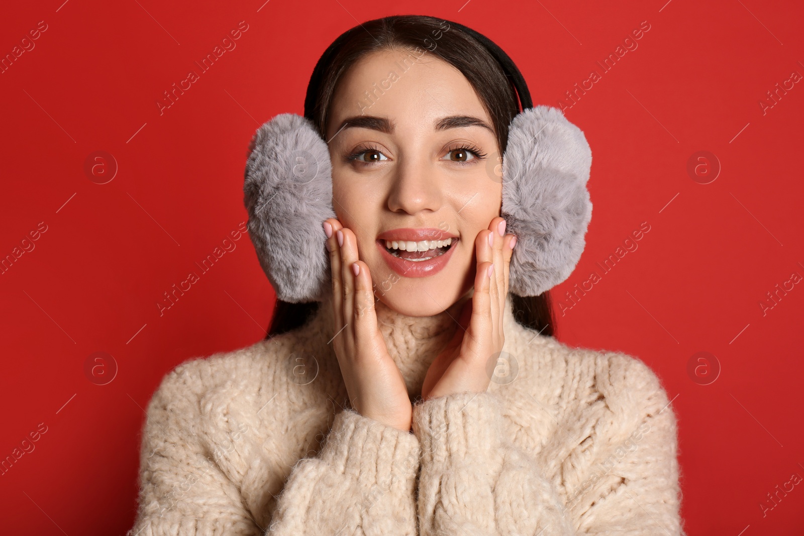 Photo of Beautiful young woman wearing earmuffs on red background