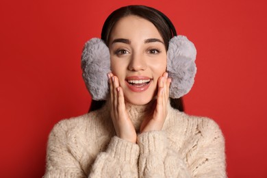 Photo of Beautiful young woman wearing earmuffs on red background