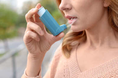 Image of Woman using asthma inhaler outdoors, closeup. Health care