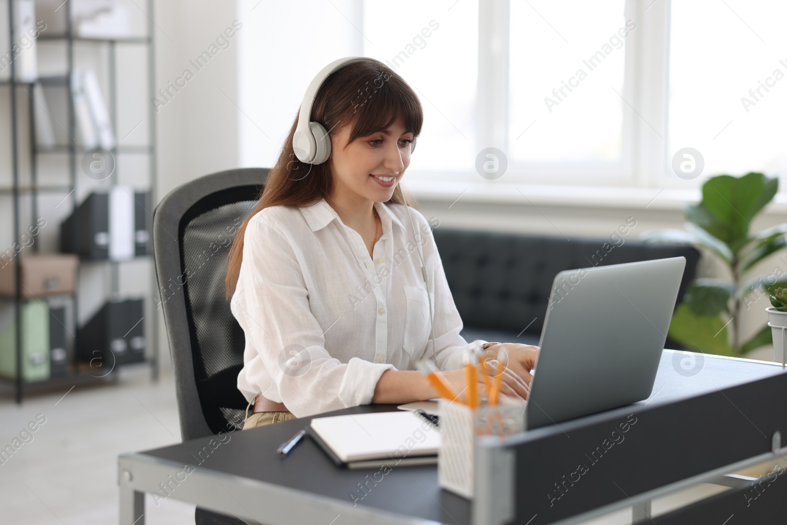 Photo of Woman in headphones watching webinar at table in office