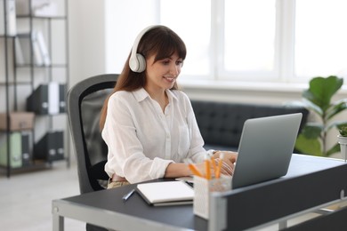 Woman in headphones watching webinar at table in office