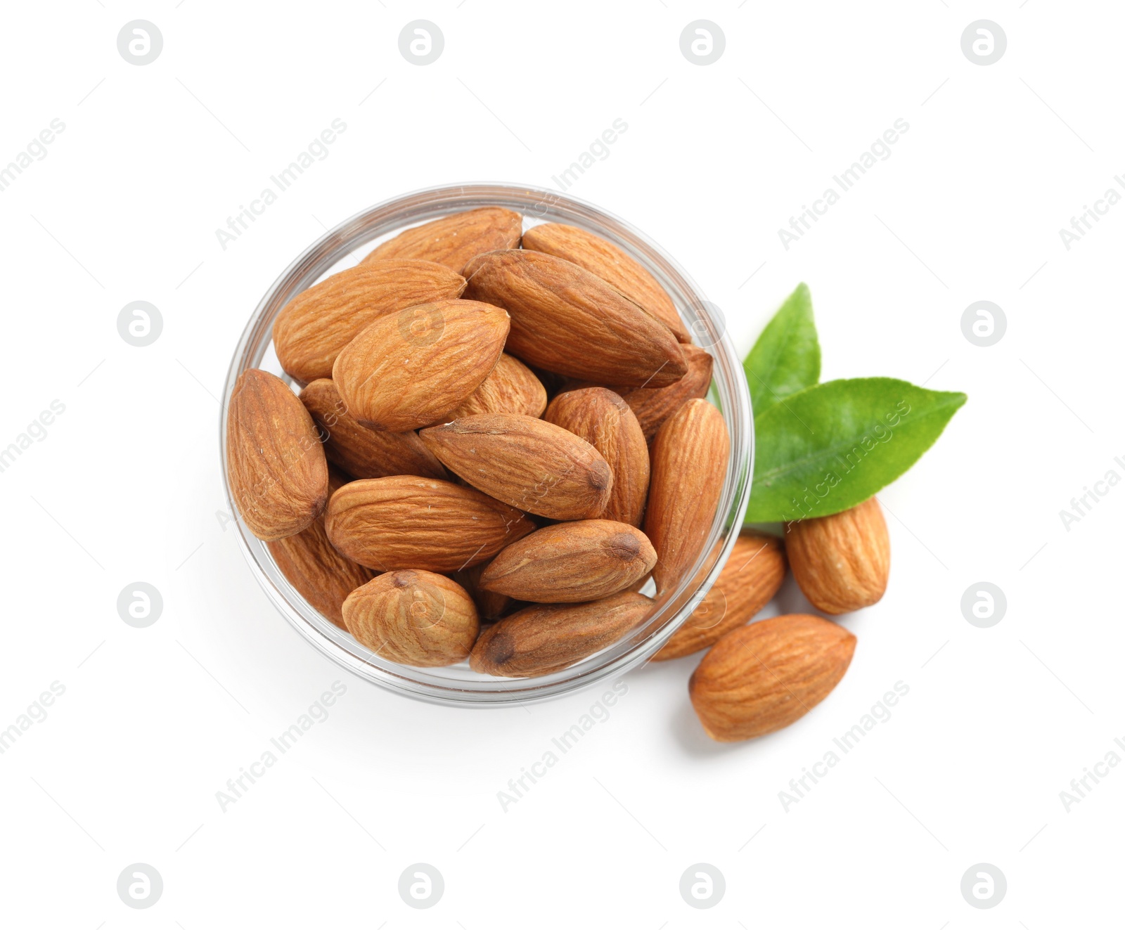 Photo of Glass bowl with organic almond nuts and green leaves on white background, top view. Healthy snack