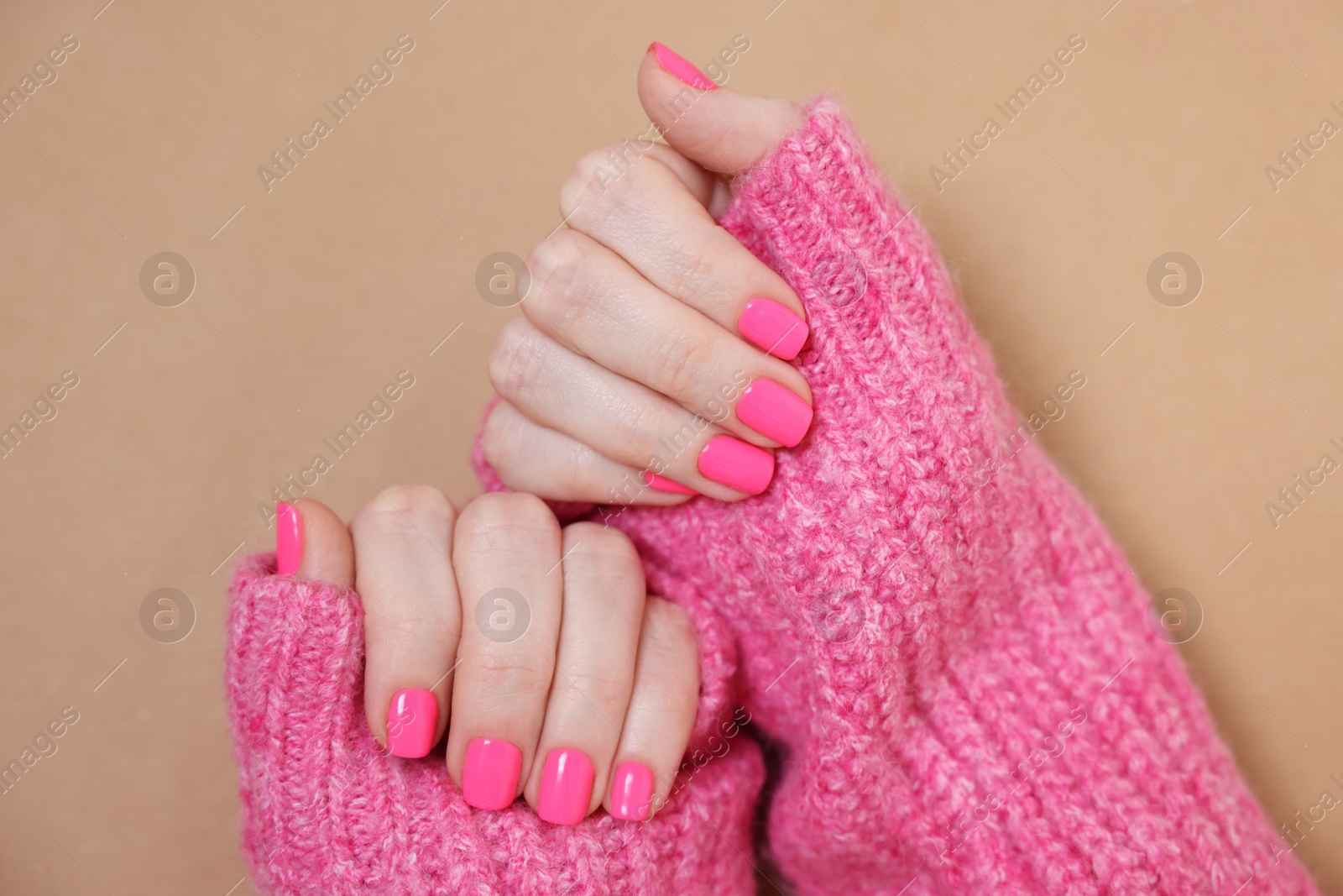 Photo of Woman showing her manicured hands with pink nail polish on dark beige background, top view