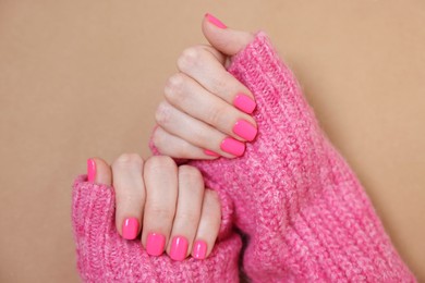 Woman showing her manicured hands with pink nail polish on dark beige background, top view