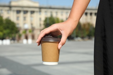 Photo of Woman holding takeaway cardboard coffee cup with plastic lid outdoors, closeup