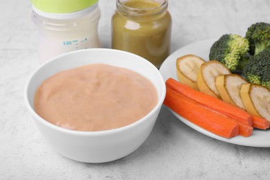 Bowl with healthy baby food and ingredients on white table, closeup