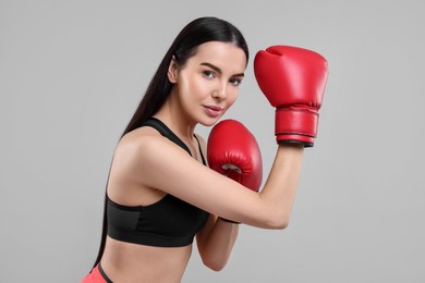 Portrait of beautiful woman in boxing gloves on grey background