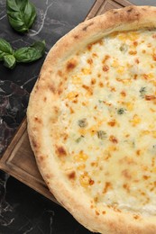 Delicious cheese pizza and basil on black marble table, flat lay