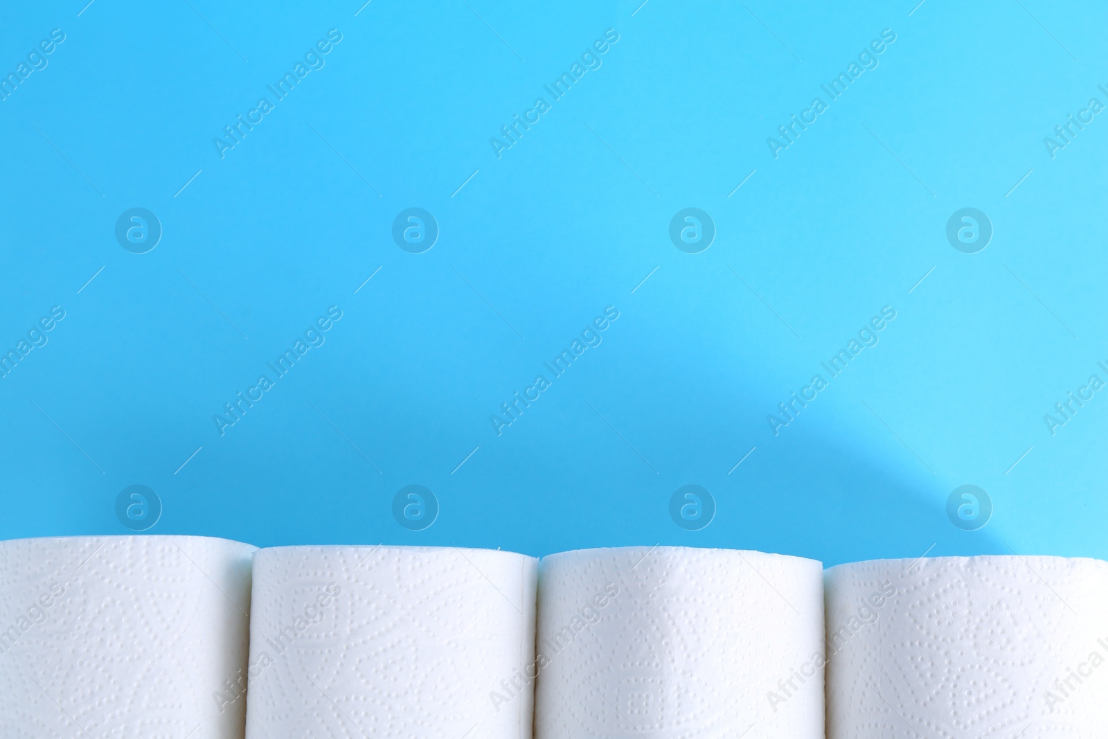 Photo of Soft toilet paper rolls on light blue background, flat lay. Space for text