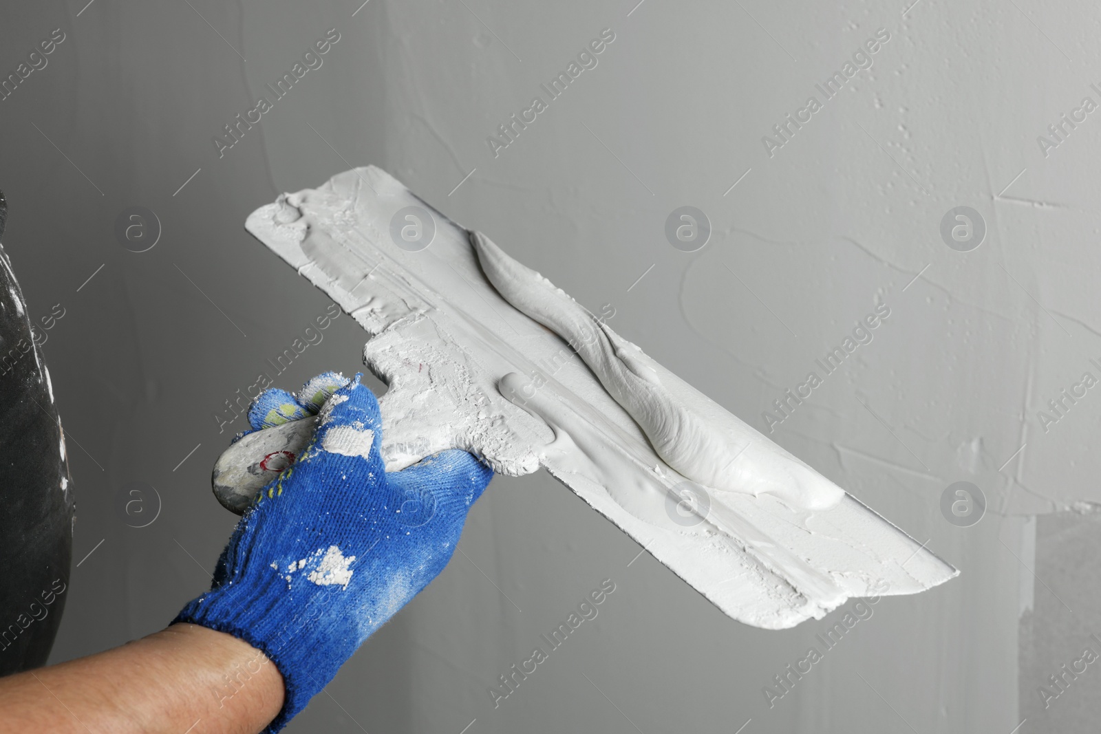 Photo of Professional worker holding putty knife with plaster indoors, closeup