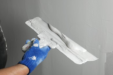 Photo of Professional worker holding putty knife with plaster indoors, closeup