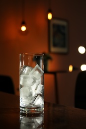 Photo of Glass with ice cubes on table in dark room