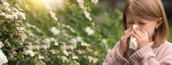 Image of Little girl suffering from seasonal pollen allergy near blossoming tree on spring day. Banner design with space for text