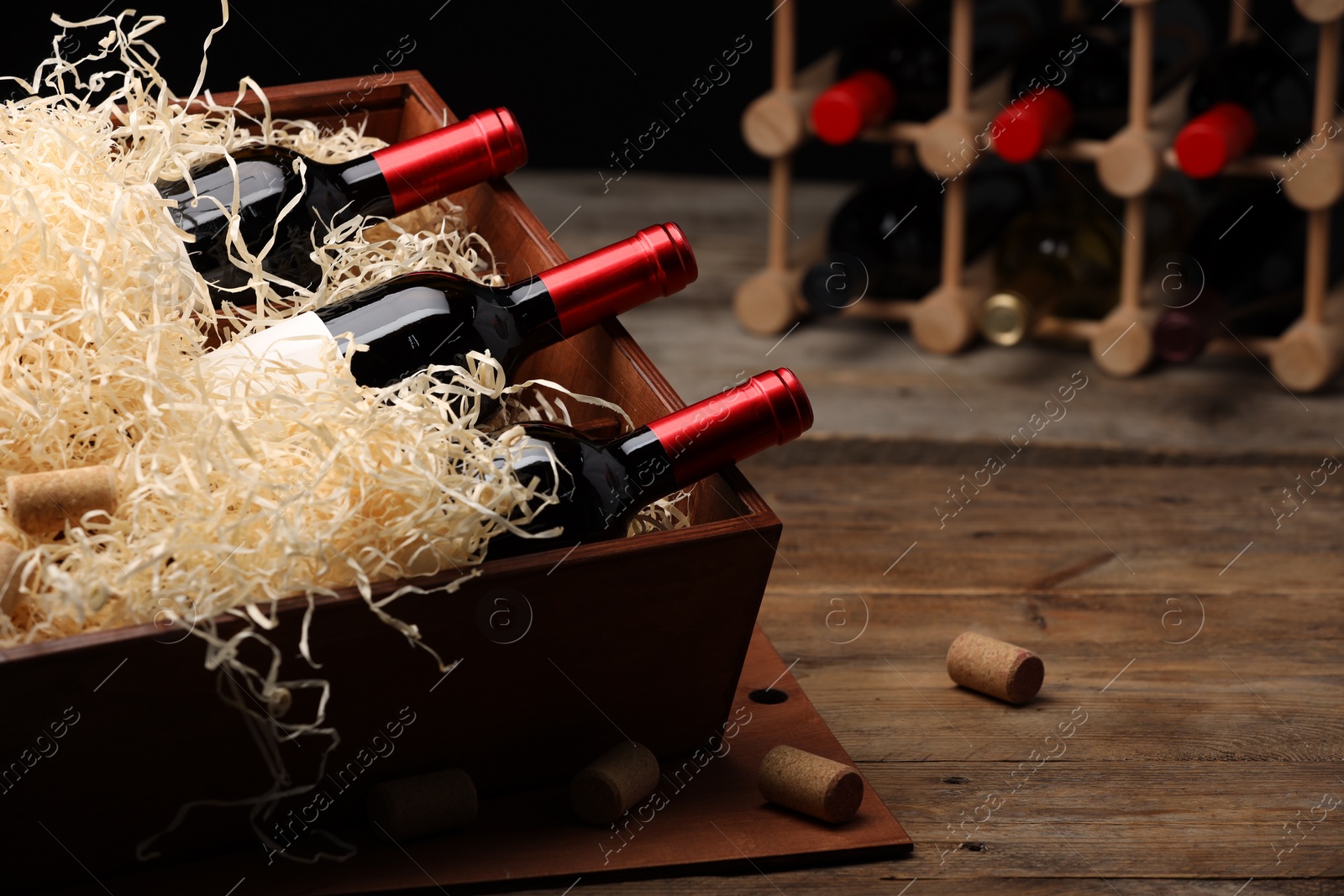 Photo of Box with wine bottles on wooden table against black background. Space for text