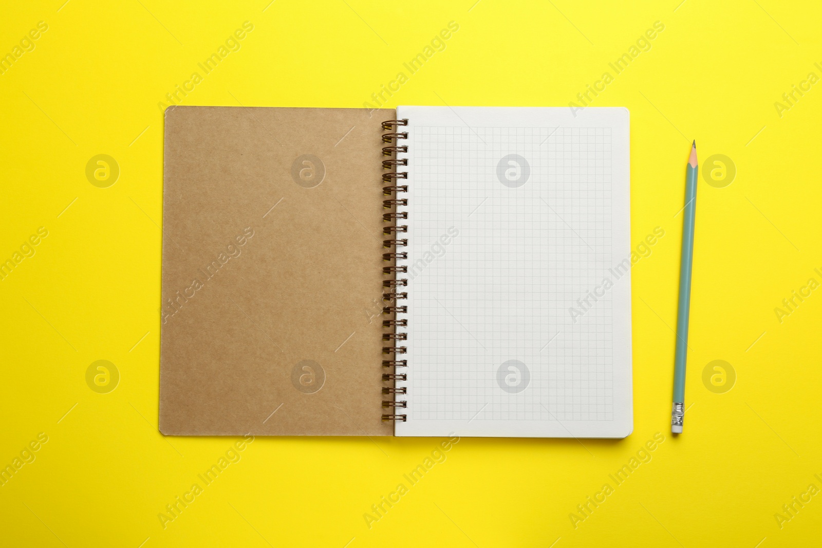 Photo of Notebook and pencil on yellow background, top view