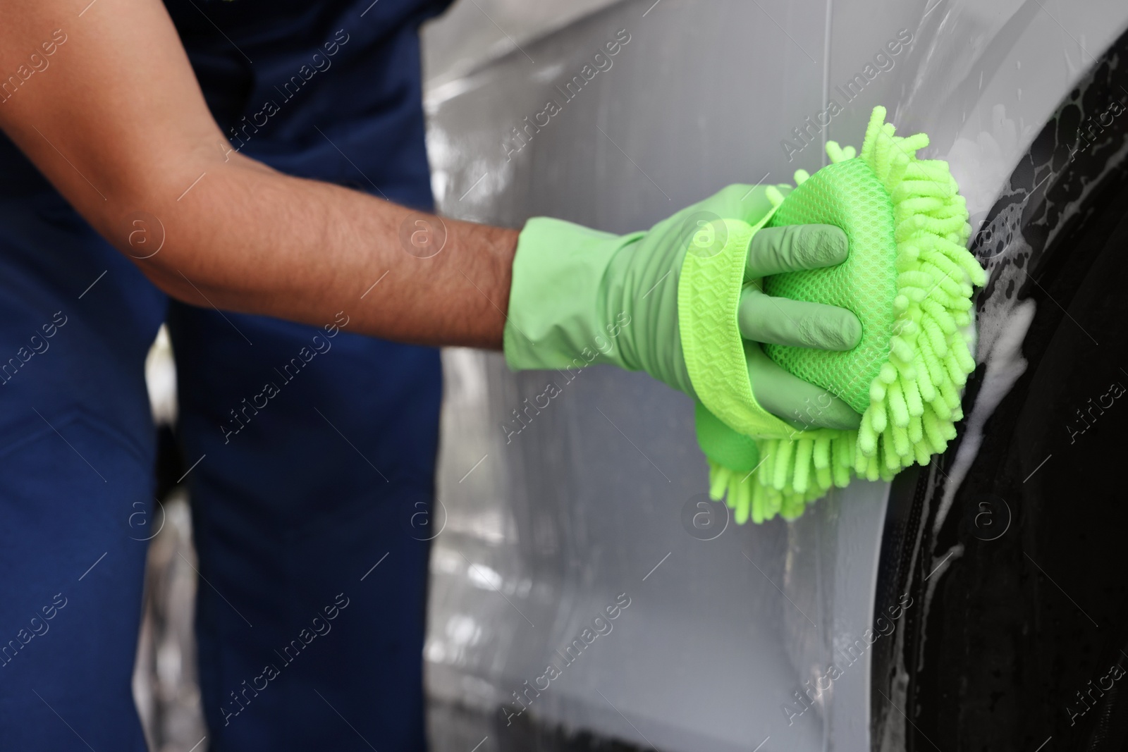 Photo of Worker in rubber gloves washing car with sponge, closeup