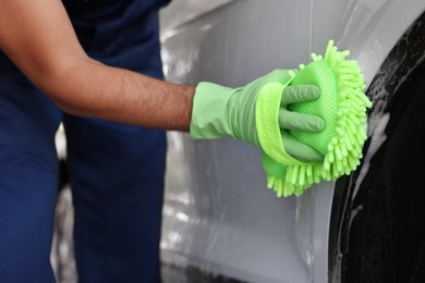 Photo of Worker in rubber gloves washing car with sponge, closeup